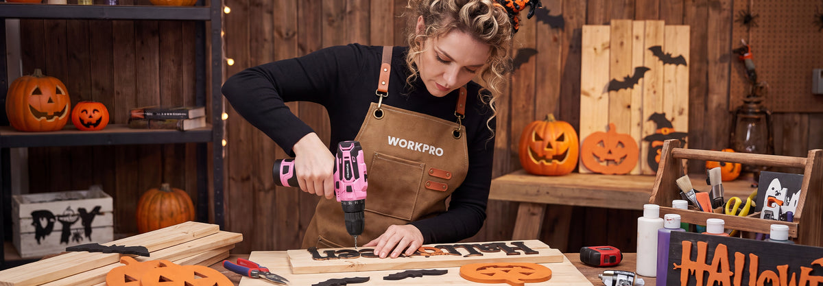 Woman using a cordless drill to assemble a wooden Halloween decoration at a workshop table
