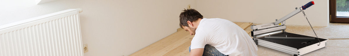 Man installing a white radiator beside a black and silver floor hatch in a bright room