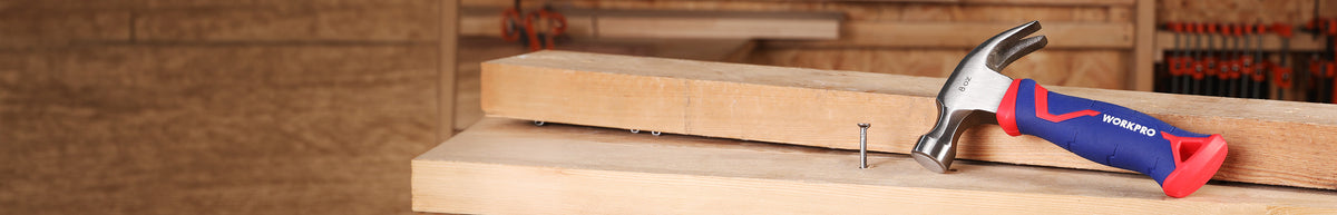 Hammer with a red and blue handle resting on a wooden workbench beside a small nail