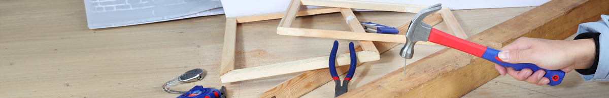 Hands use red handled pliers and a hammer to assemble a wooden frame on a workshop bench