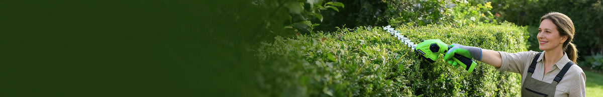 Gardener using green pruning shears to trim a leafy hedge, with dense foliage and a person wearing protective gloves
