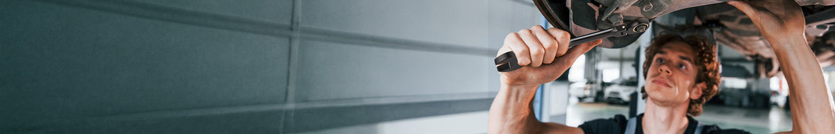 Worker using a cordless drill to fasten a metal panel overhead in an industrial interior