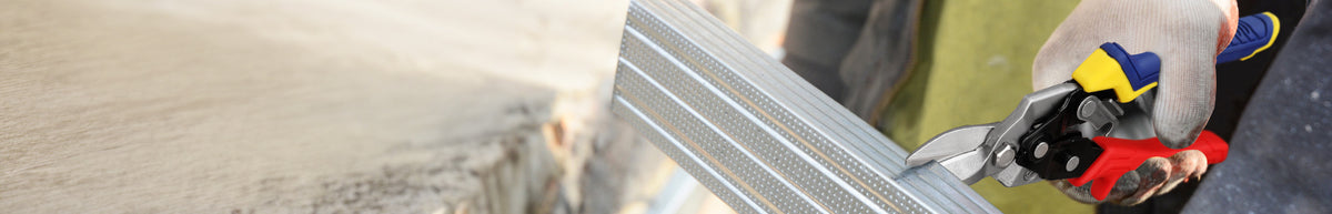 Gloved hand using pliers to cut several parallel metal wires beside a rough concrete surface