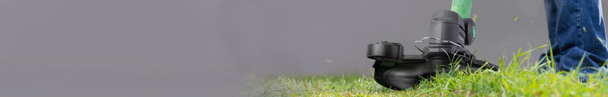 String trimmer cutting green grass beside a person's blue jeans, with the black cutting head visible