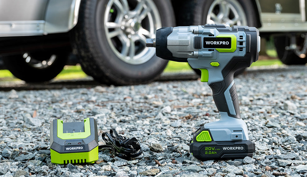 Cordless impact wrench with 20V battery, charger, and power cord on gravel beside a parked vehicle