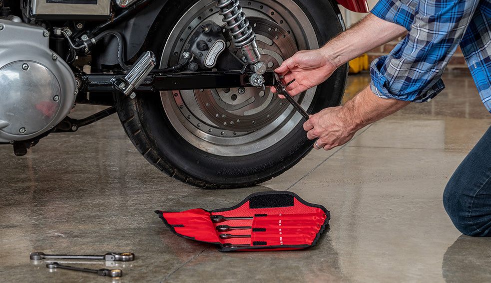 Motorcycle maintenance with a mechanic adjusting the rear wheel, brake disc, and suspension using hand tools