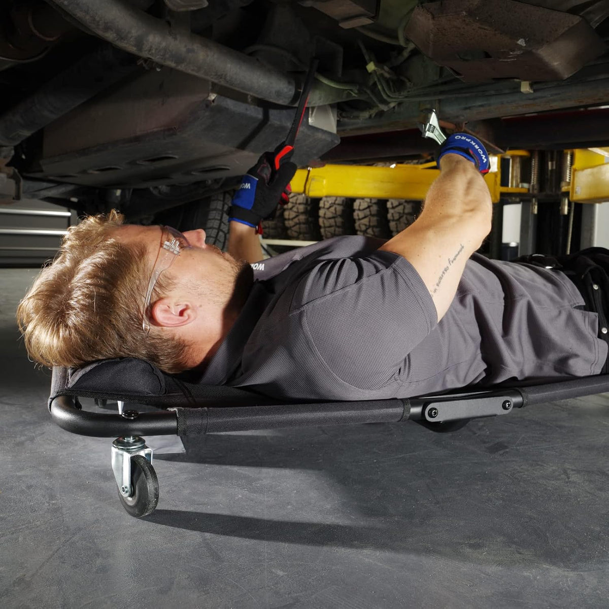 Workpro foldable automotive creeper in black with a mechanic working beneath a vehicle during repair