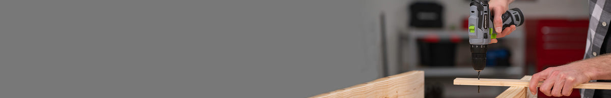 Cordless drill held above a wooden board as a person works at a workshop bench