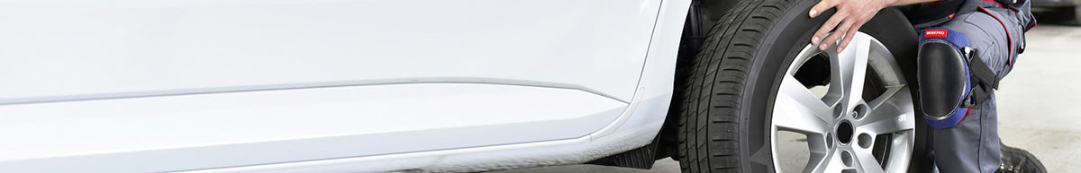 Person in protective workwear inspecting a car wheel and tire beside a white vehicle