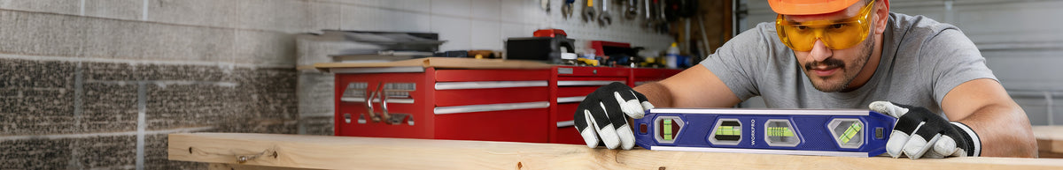 Worker wearing safety glasses uses a blue spirit level on a wooden workbench in a workshop