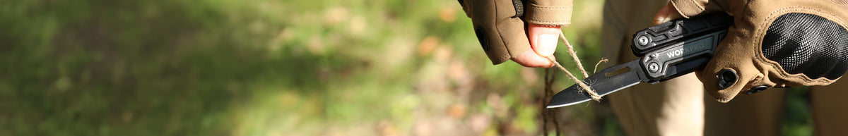 Close view of a person wearing brown protective gloves and holding a compact black outdoor tool against a blurred green