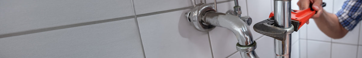 Plumber using a red adjustable wrench on a chrome pipe fitting against a tiled wall