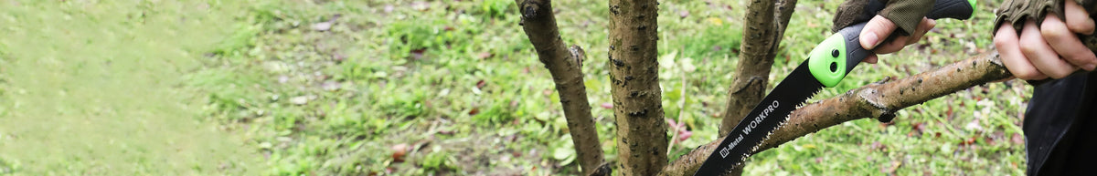 Handheld pruning shears cutting a tree branch in a grassy outdoor setting with green handles
