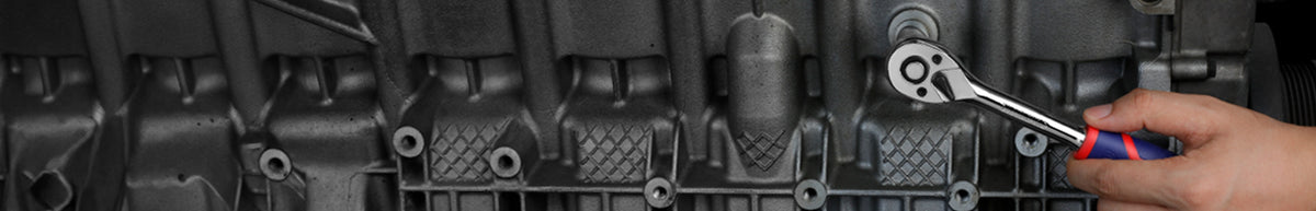 Mechanic using a ratchet and screwdriver on a dark metal engine assembly, with visible bolts and ribbed components