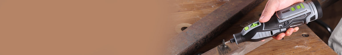 Cordless drill with a battery pack drilling into a dark wooden plank on a workbench