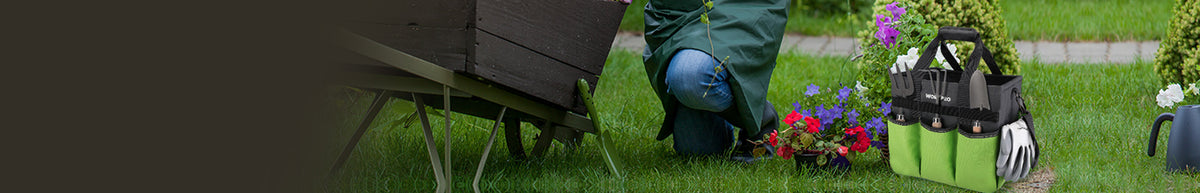 Gardening tools and supplies beside a flower bed, including a green tool bag, gloves, kneeling pad, and wheelbarrow