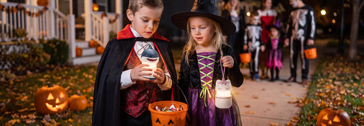Children in Halloween costumes carry a glowing pumpkin bucket and lantern on a decorated neighborhood street