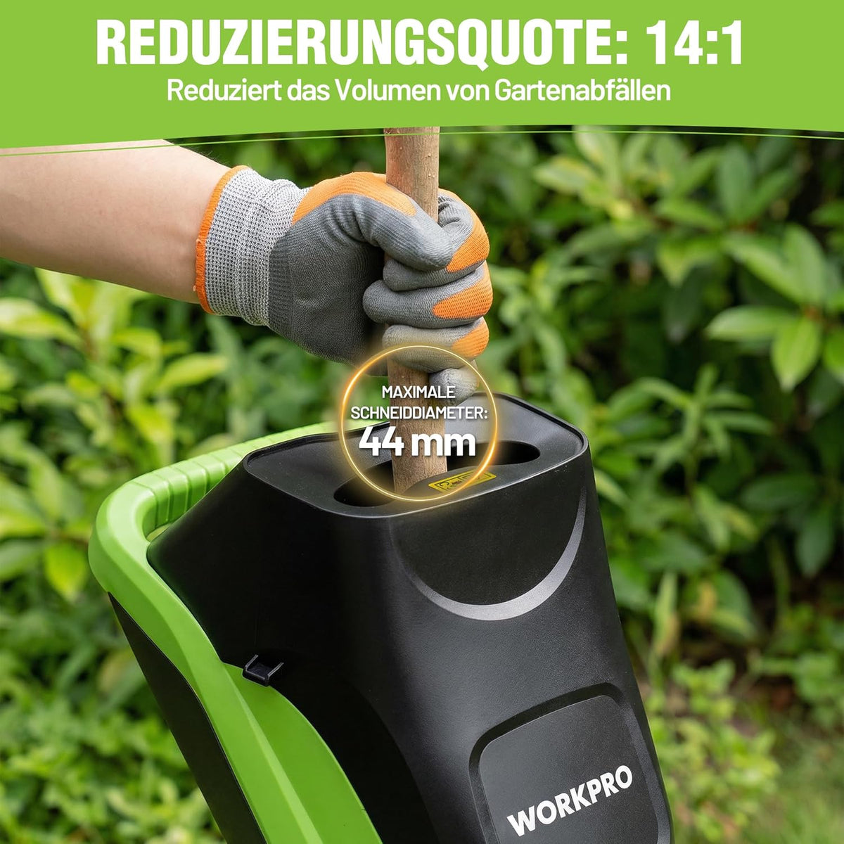Electric garden shredder hopper being fed by gloved hand with branches