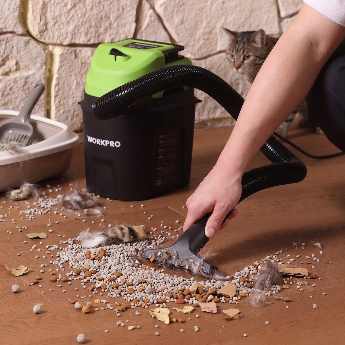 Wet/dry vacuum with green lid and black tank used with a floor nozzle, clearing debris.