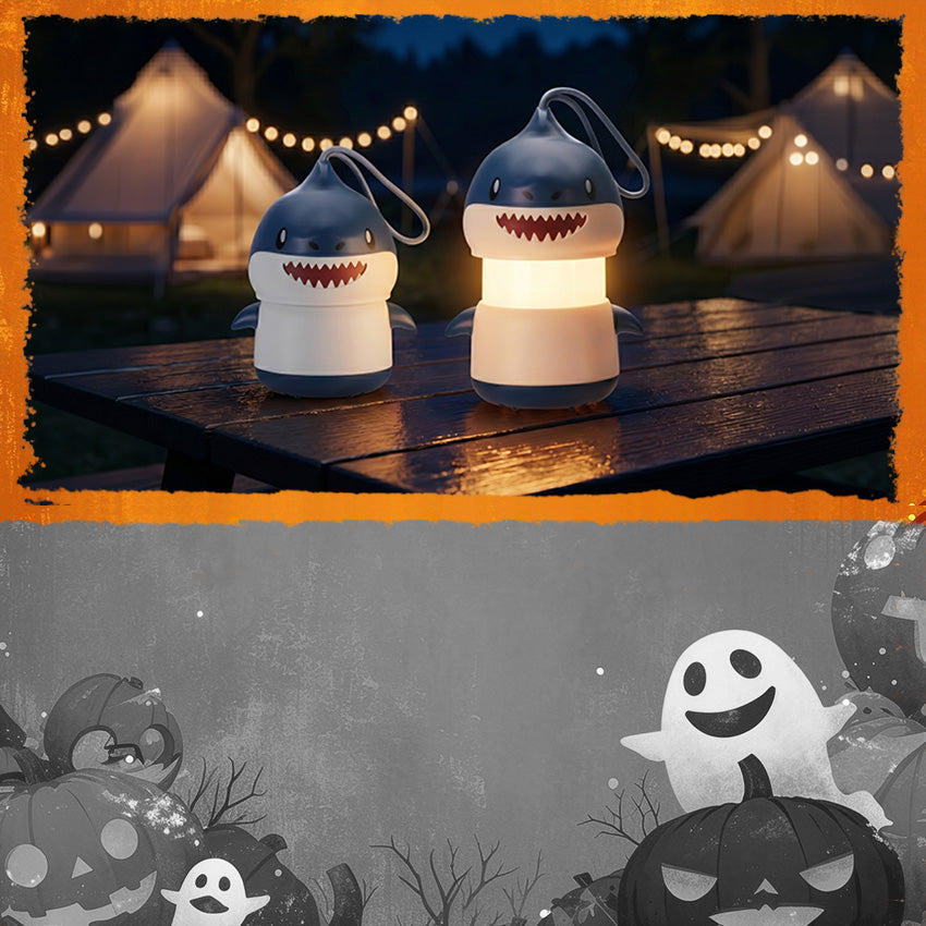 Two shark shaped lanterns with glowing lights sit on a wooden table at night beside illuminated camping tents