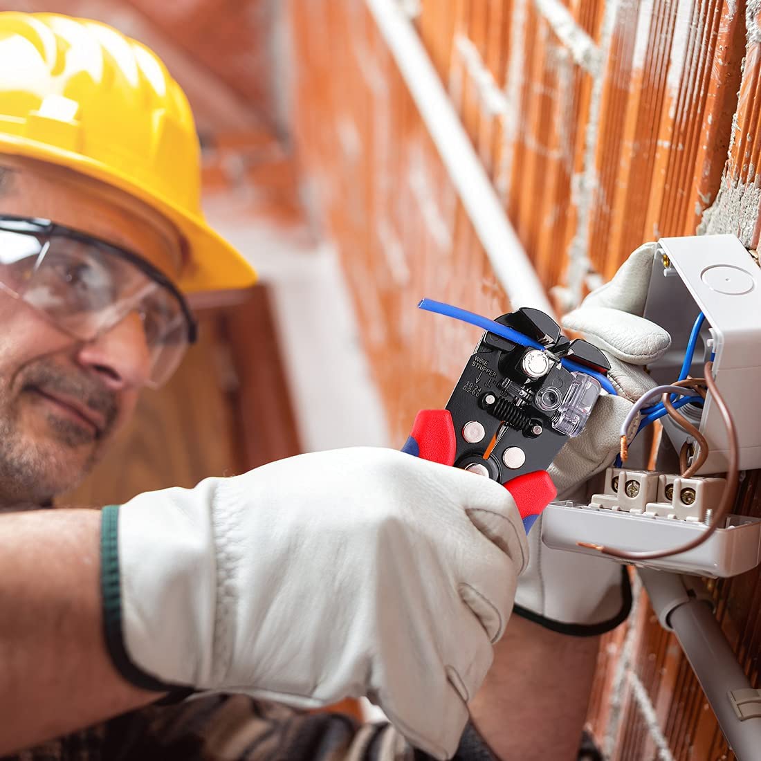 Wire stripper clamped on electrical wires inside a terminal box, technician wearing gloves