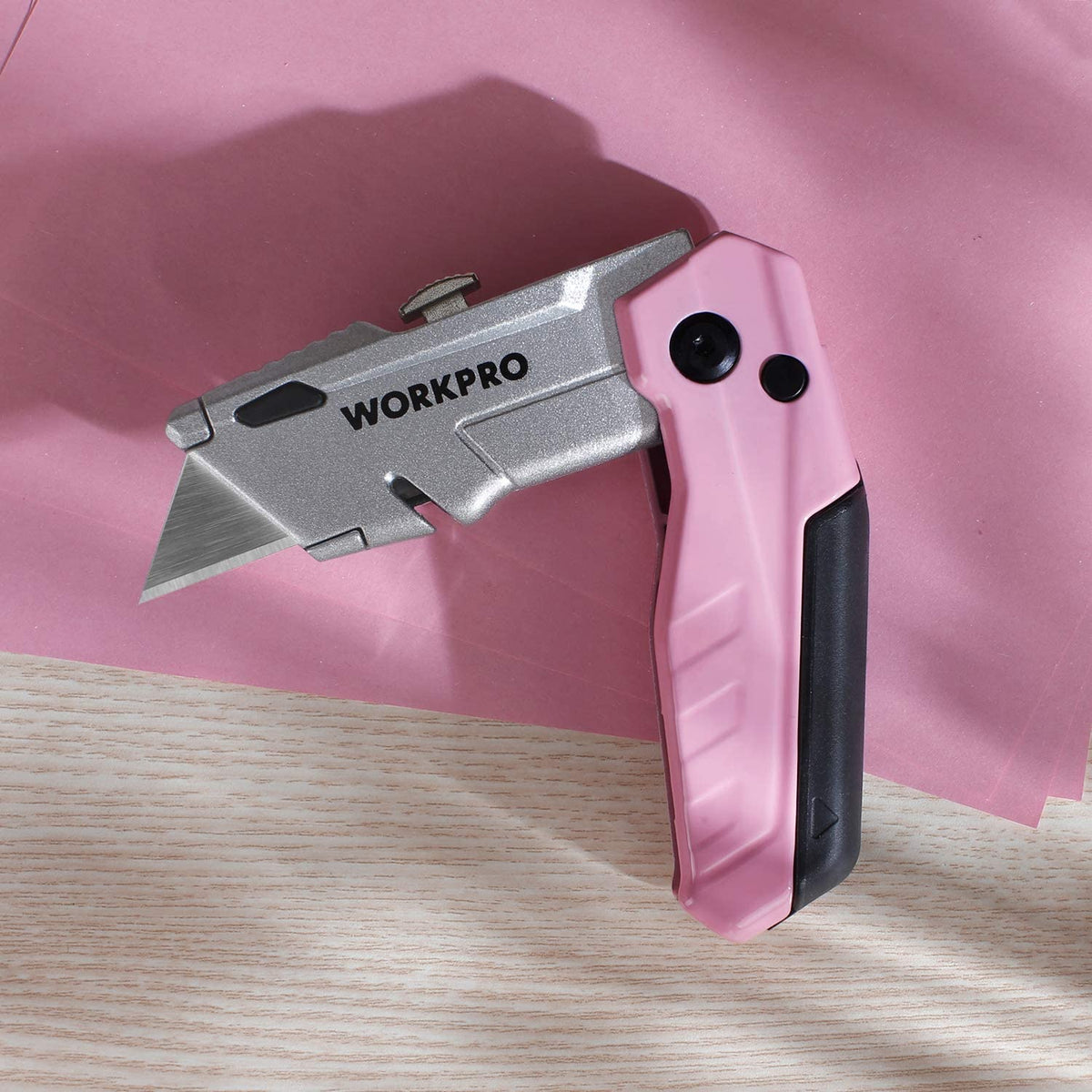 Pink folding utility knife with grey blade cutting along a light wood surface